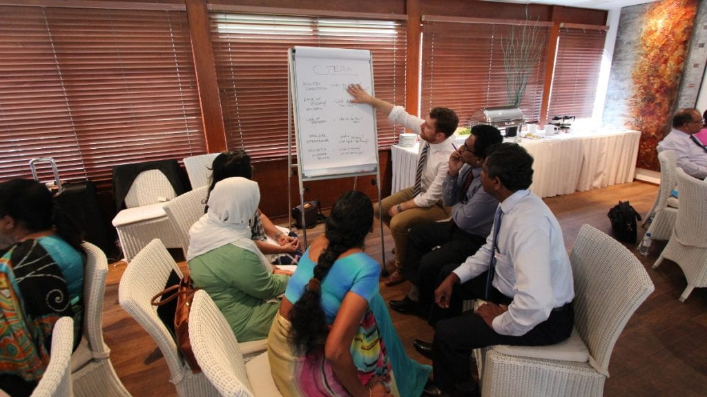 Peter Harrington pointing to a white board with participants from Sri Lanka seated in a circle