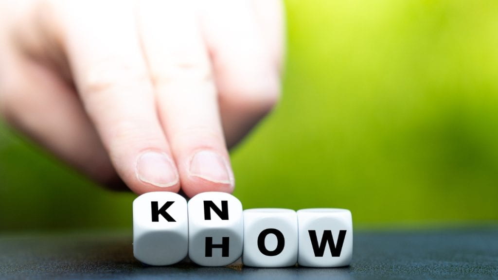 A hand moving dice with letters that spell "KNOW" on one side and "HOW" on another