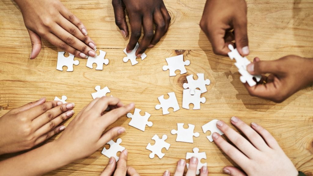 Several hands reaching toward puzzle pieces in the center of table