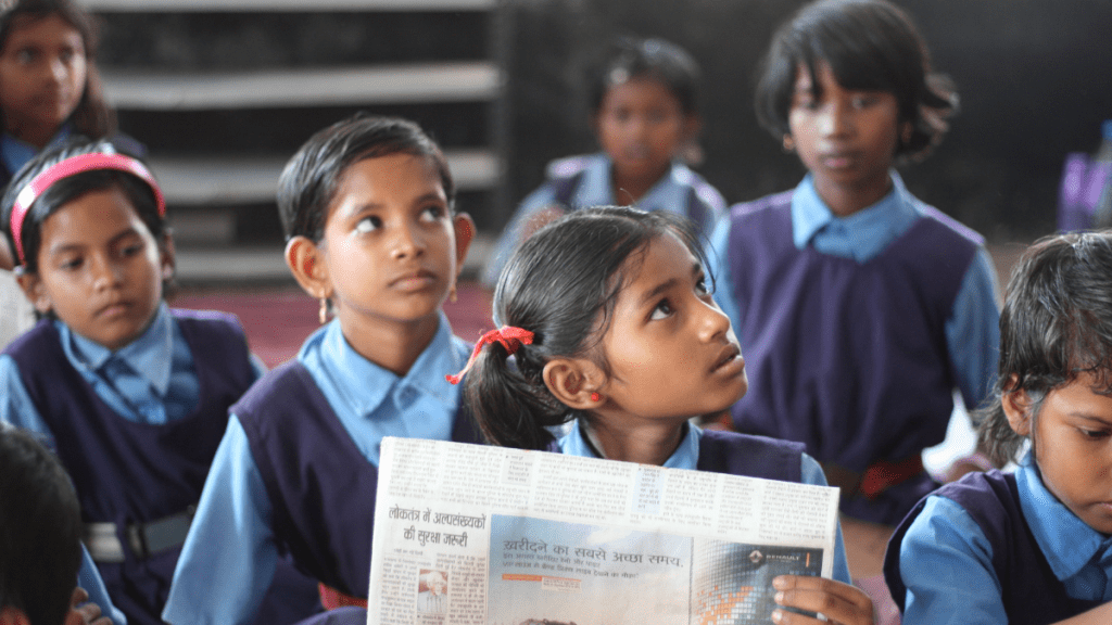 Child holding a newspaper sitting with other children