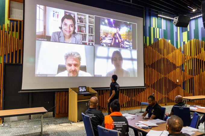 Matt Andrews and Salimah Samji projected on screen teaching