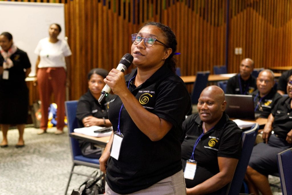 PNG participant holding microphone and talking with seated participants in the background