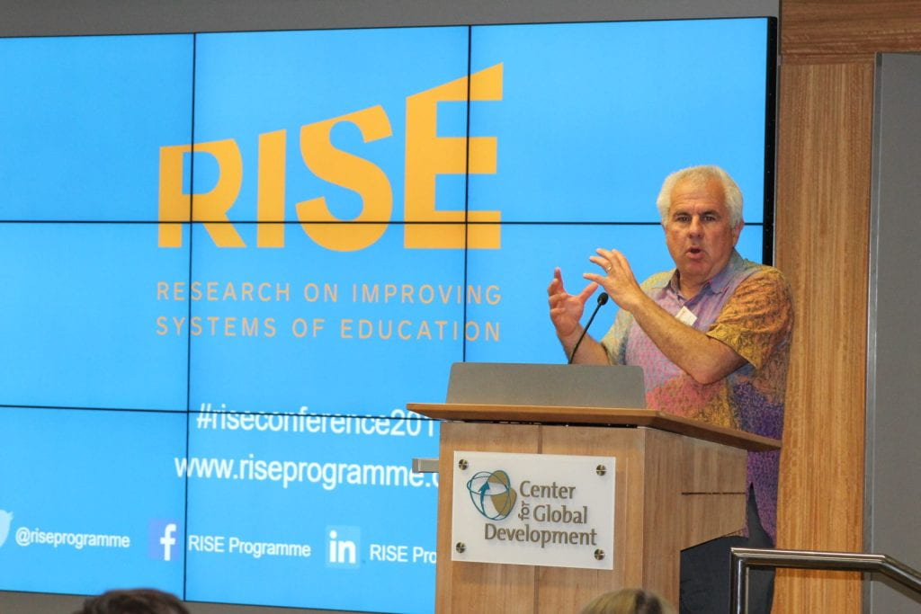 Lant Pritchett presenting in front of a light blue slide with "RISE" written in yellow
