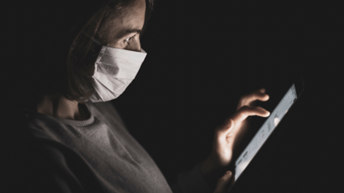A person wearing a mask and looking at a phone screen