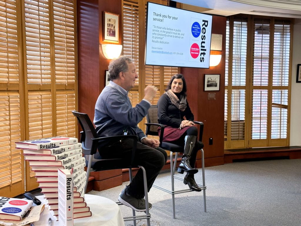 Steve Kadish speaking to audience with Salimah Samji in the background and his Results book stacked in the foreground