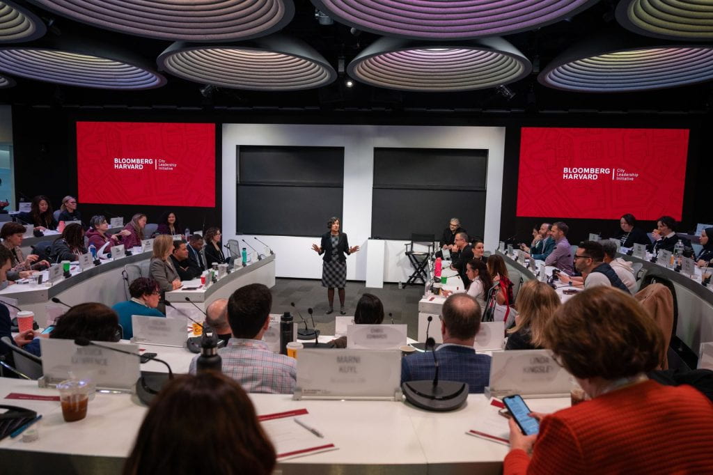 Salimah Samji teaching in a large auditorium with large Bloomberg Harvard slides in background