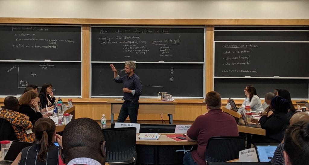Matt Andrews teaching in front of a classroom of students and several chalkboards with notes behind him