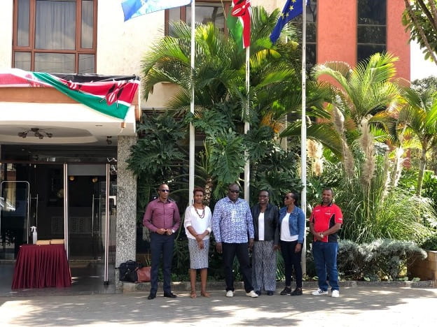PDIA for Education Systems Kenya project team standing in front of a hotel with Kenyan flag