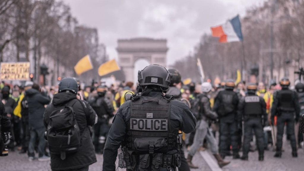 Police officers approaching a crowd with French flag in background