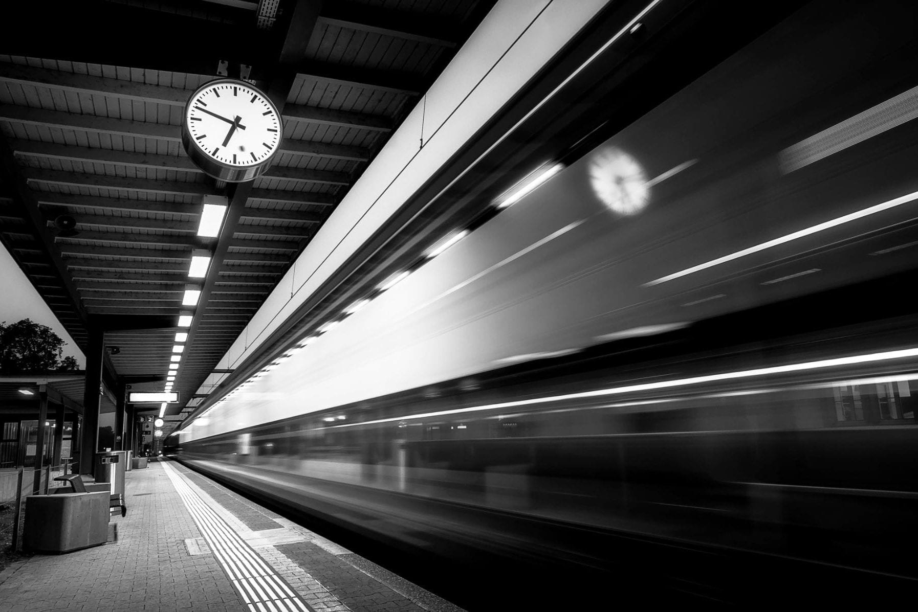 A clock on a train platform with train speeding by