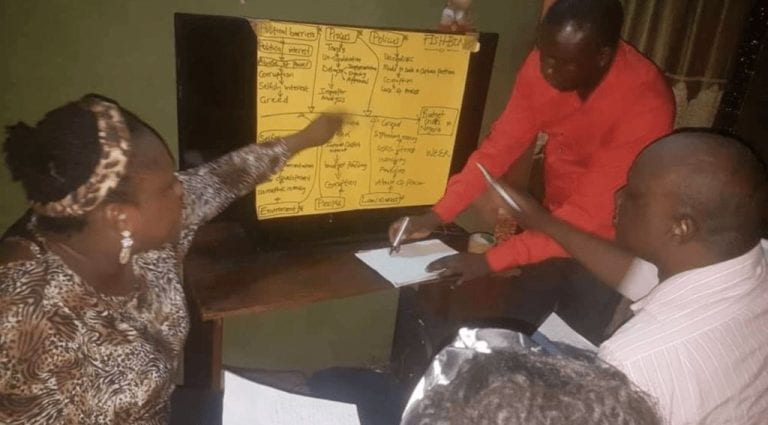 two people working over a yellow chart paper on a wall