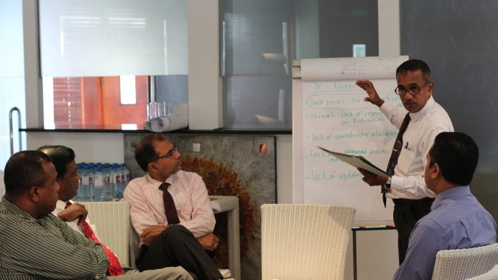 Sri Lanka participant talking and standing in front of a whiteboard with group members listening