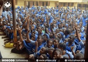 a crowd of school girls in a yard raising their hand
