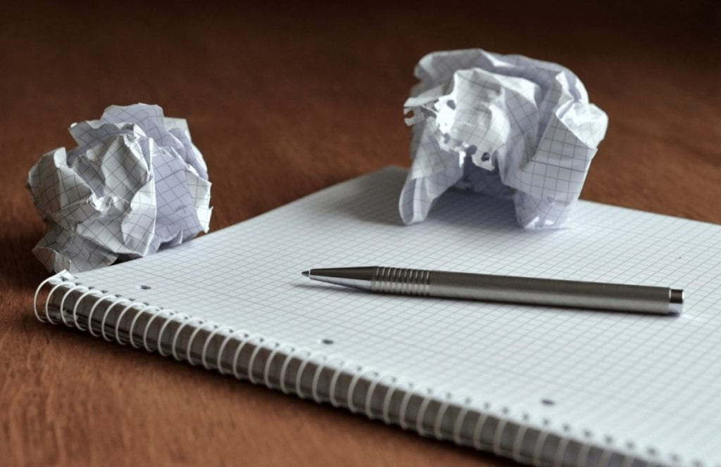Pen and notepad on a desk with two balls of crumpled paper on the notepad