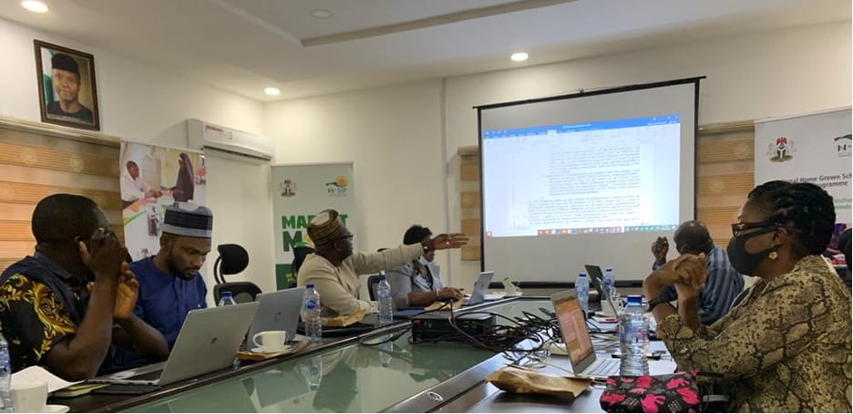A group of people at a table listening to a presentation and looking at projected slides