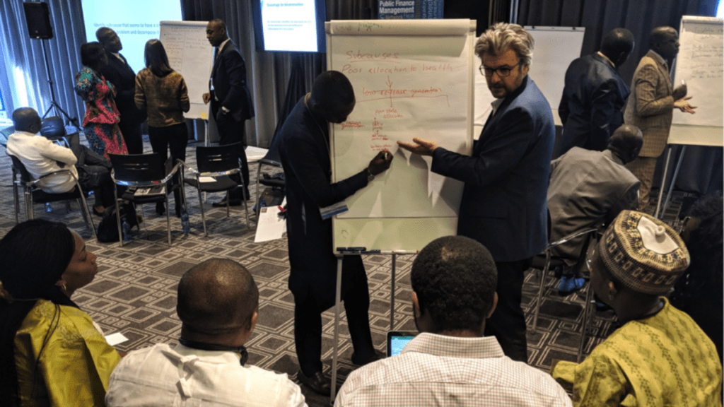 Matt Andrews teaching a group and pointing to a whiteboard