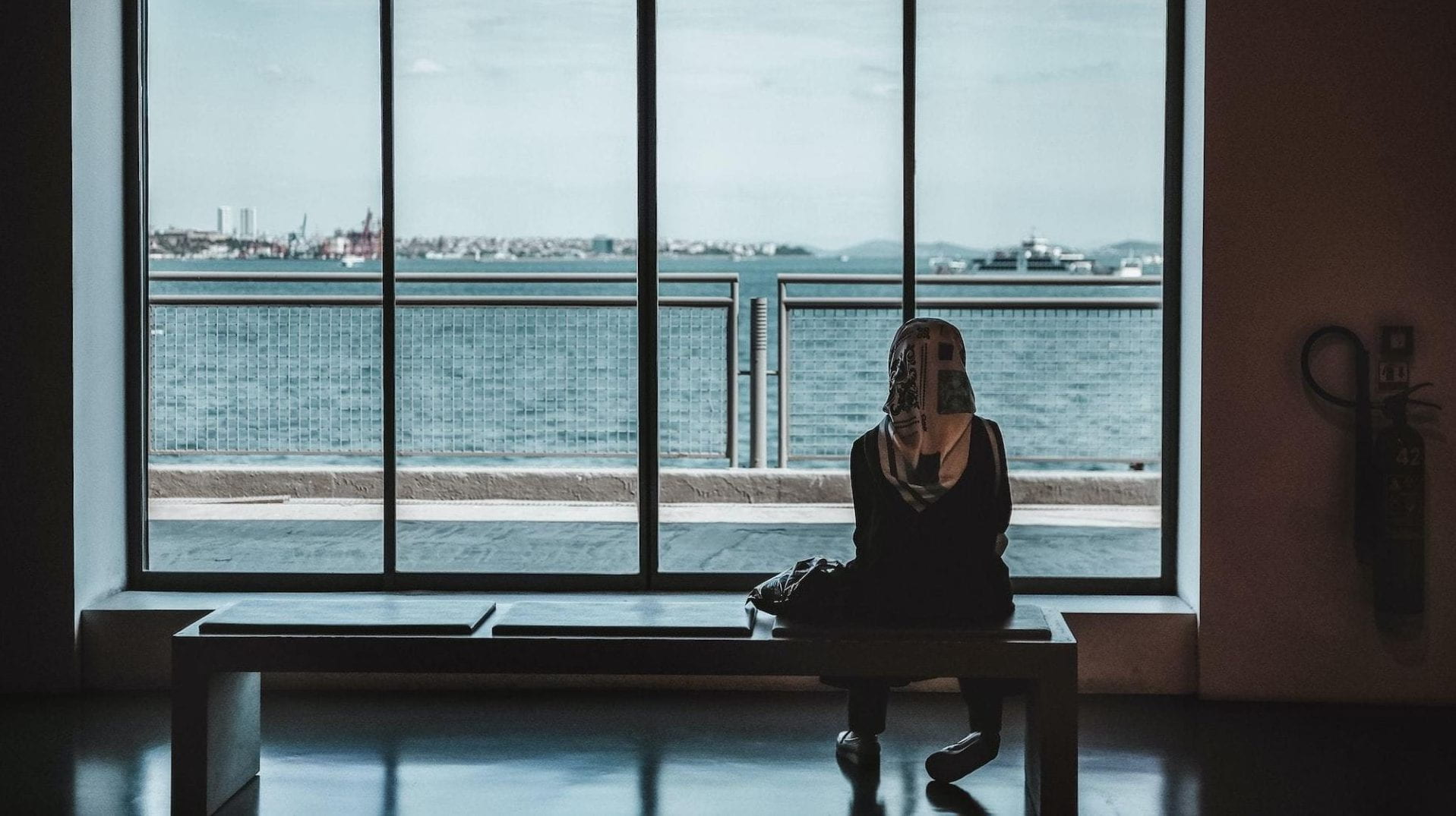 A person seated and looking out a window to the ocean