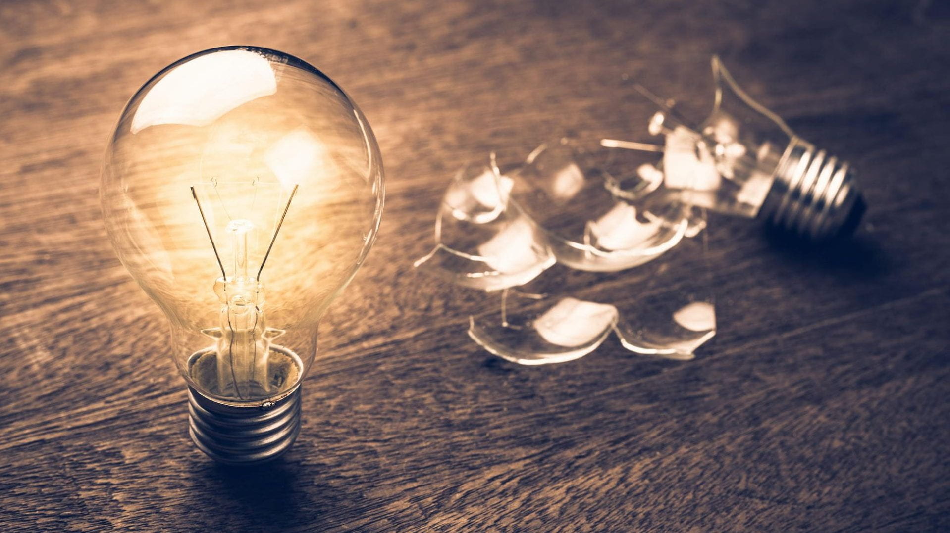A lightbulb on a table with a broken one next to it