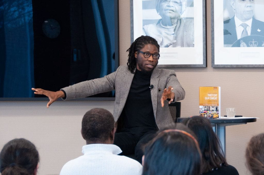 Daniel Agbiboa talking to students with his book "They Eat Our Sweat" on table