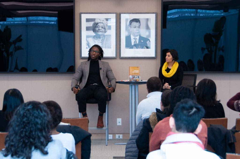 Daniel Agbiboa talking to students with his book "They Eat Our Sweat" on table. Salimah Samji seated adjacent