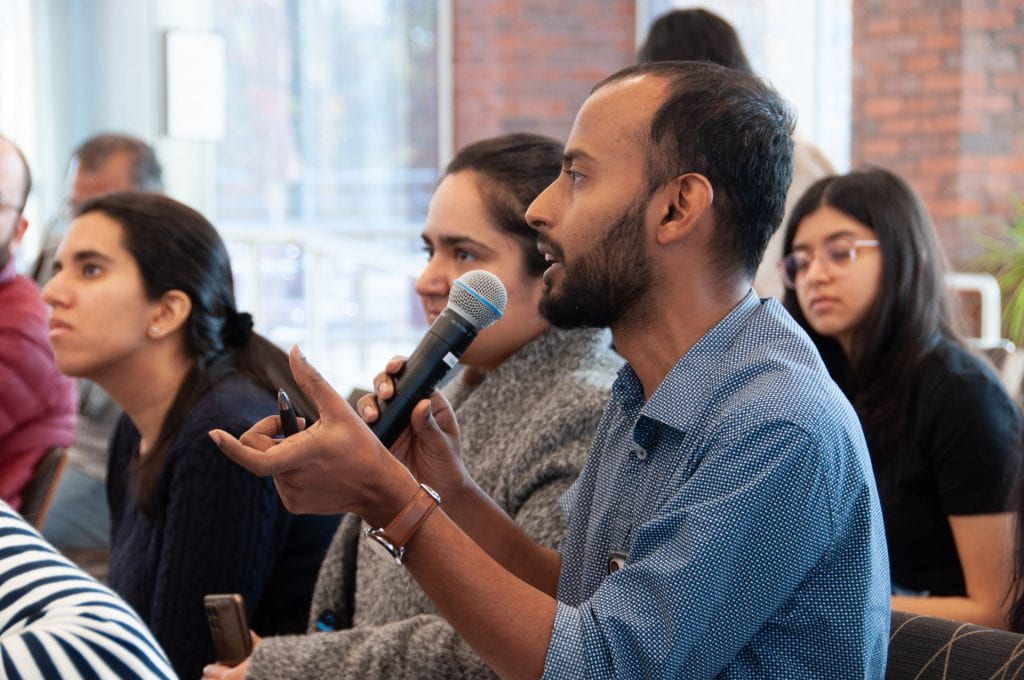 Audience member holding microphone and asking a question with students in the background