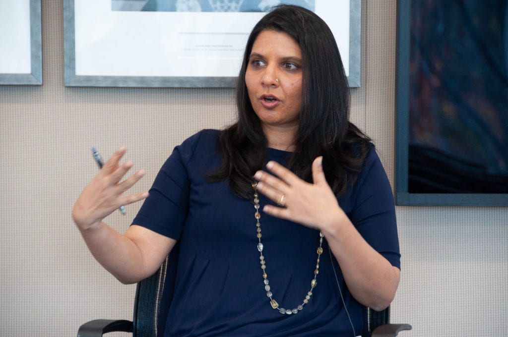 Yamini Aiyar wearing black and a long necklace and presenting using her hands to motion