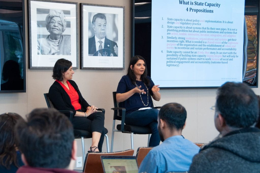 Yamini Aiyar and Salimah Samji seated and presenting as panelists with students in soft focus in the foreground