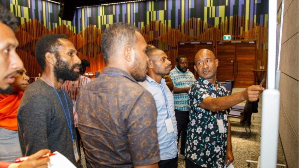 PNG group photo with one participant pointing at white board
