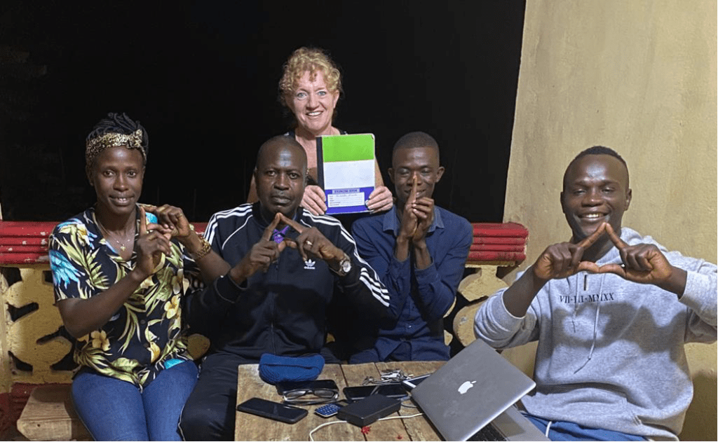 Sierra Leone team seated and smiling and each spelling the letters P-D-I-A with their hands