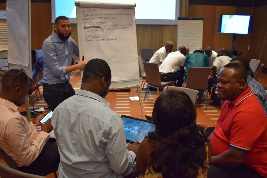 Ghana team in a semicircle while one team member talks and points to white board