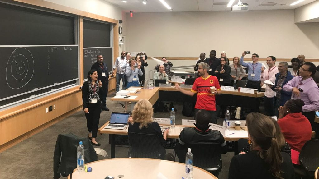 Participants in a classroom throwing airplanes toward a bullseye target on the chalkboard