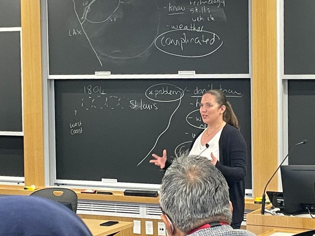 Ivana speaking to students with notes on the blackboard behind her