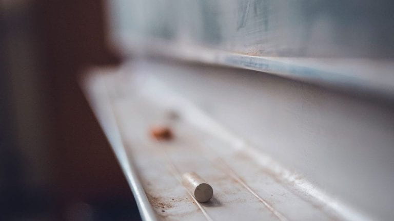 A piece of chalk on shelf of chalkboard