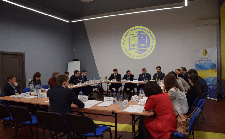 Professionals at a roundtable with a projection of a Ukrainian legal logo on the wall