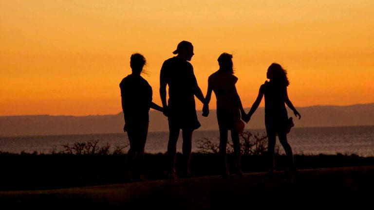 Adults and children hold hands on a beach in Mexico at sunset