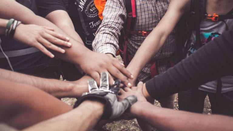 9 anonymous arms/hands reach towards eachother/touch as if they are going to say a chant as a team