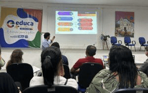 a man pointing to the slides projected on a screen as he gives a presentation to a room full of people