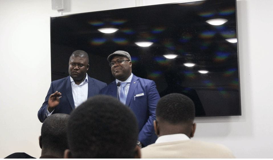 two men standing in front of a room addressing them