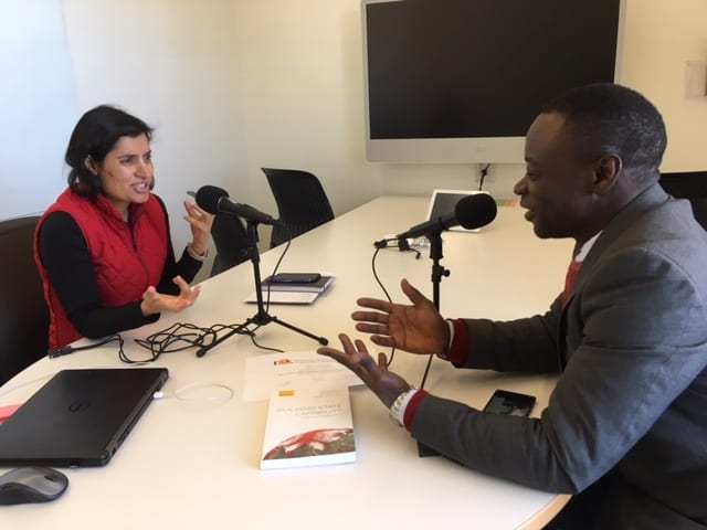 Two people speaking into a mic for a podcast