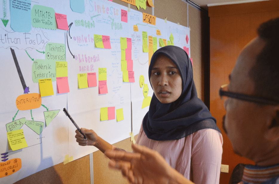 woman pointing to whiteboard with sticky notes on it