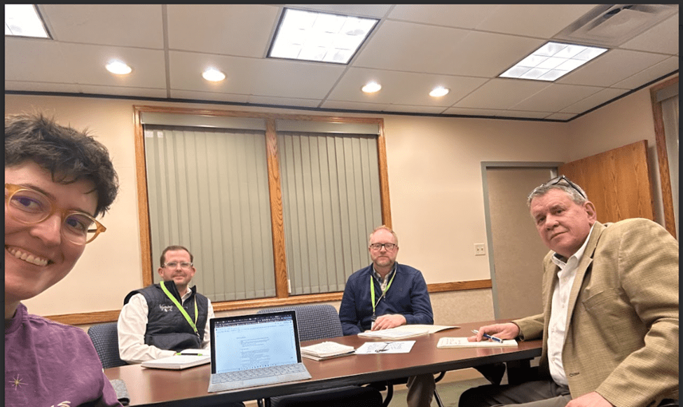 The Wild Optimists sit around a table in a meeting room