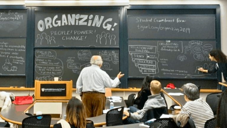 Marshall Ganz with students in front of a blackboard