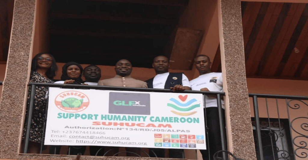 People posing on a balcony with sign "Support Humanity Cameroon SUHUCAM"