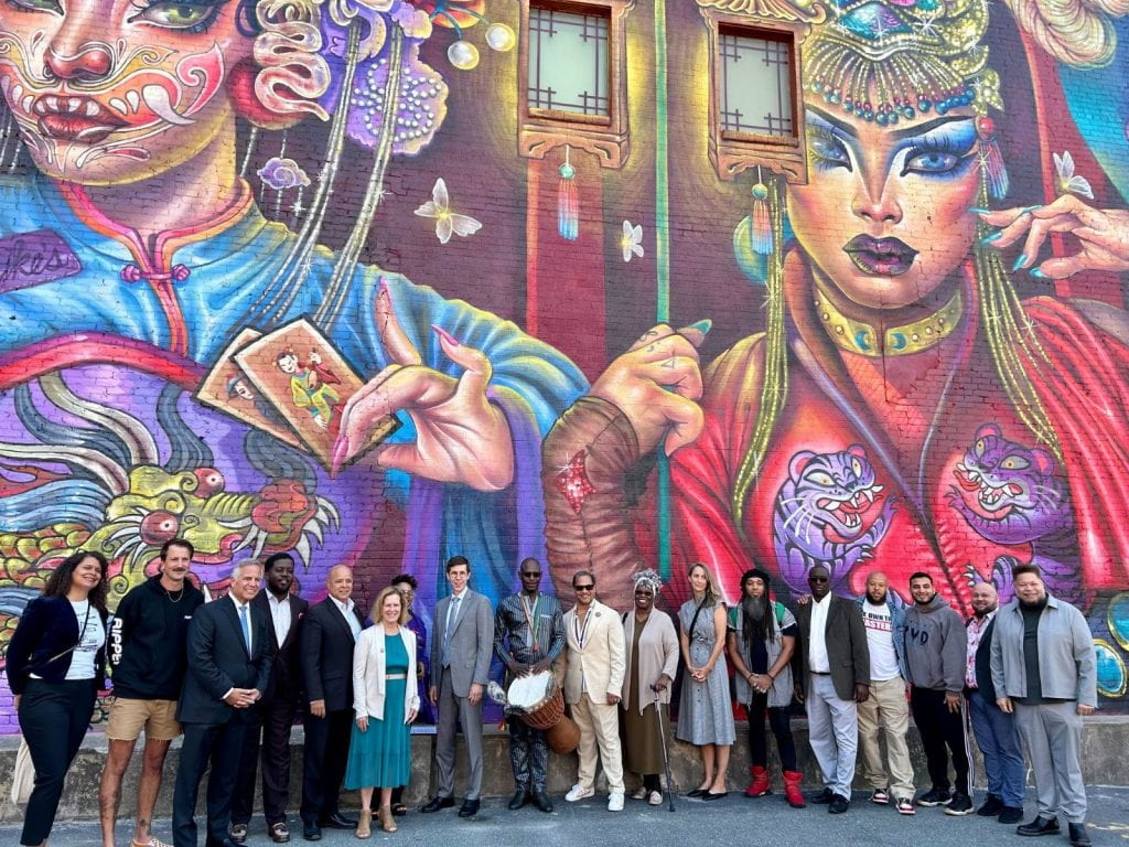 People posing with a large decorative mural on a building
