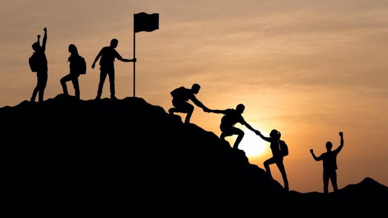 Silhouette of people helping each other climb a mountain