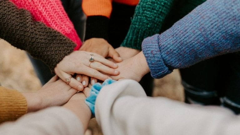 People standing in a circle with their hands on top of each other.