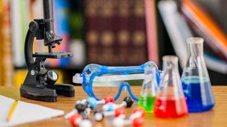 Microscope, goggles and beakers on a table.