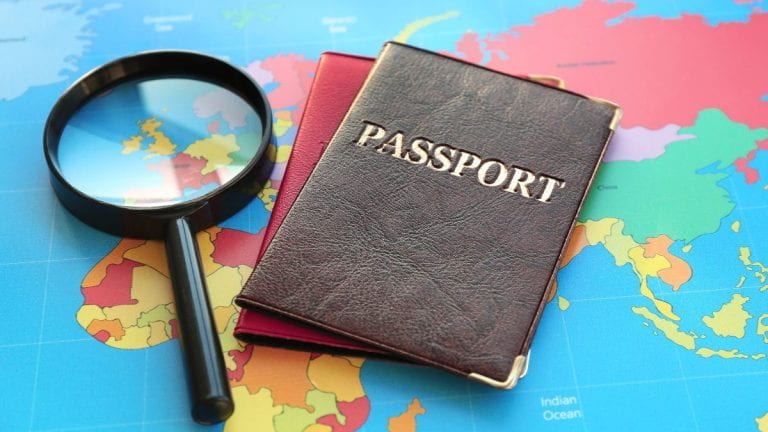 A magnifying glass and two passports rest on a colorful world map, symbolizing travel.