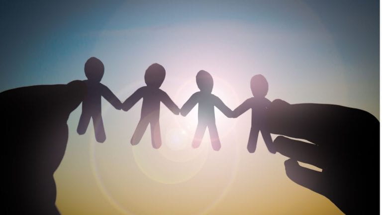 Someone holding a paper cutout of people holding hands held up against the reflection of the sun