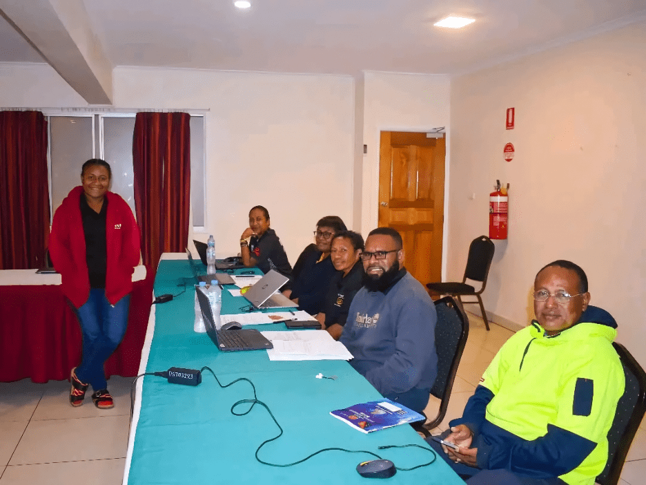 Team Edu-carers sitting at a table in a room with laptops, during a fact-finding mission in Eastern Highlands Province